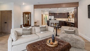 A modern living room with a sofa, armchair, and ottoman, a wooden accent wall, and a kitchen in the background. - Bavarian Mountain Suite 2 Bedroom Condo by NW Comfy Cabins by RedAwning (Leavenworth)