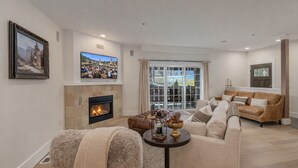 A living room with a fireplace, a sofa, a television, and a view through a glass door. - Bavarian Mountain Suite 2 Bedroom Condo by NW Comfy Cabins by RedAwning (Leavenworth)