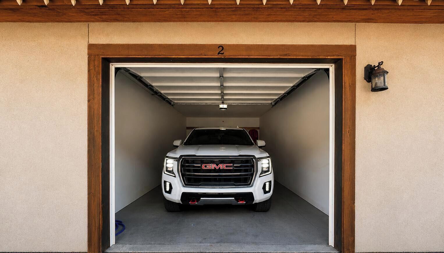 Un vehículo GMC blanco estacionado dentro de un garaje con techo de madera y el número '2' sobre la puerta.