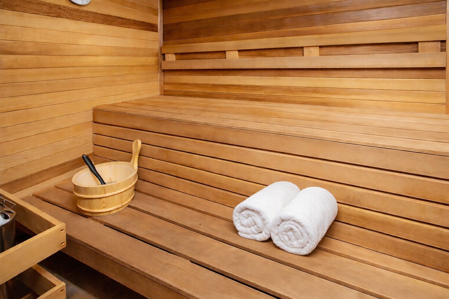 A wooden sauna with benches, a wooden bucket with a ladle, and two rolled towels.