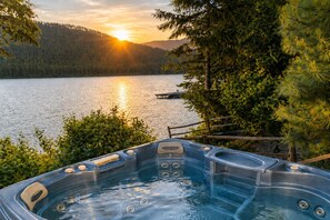 Un jacuzzi con vistas a un lago y un bosque al atardecer.