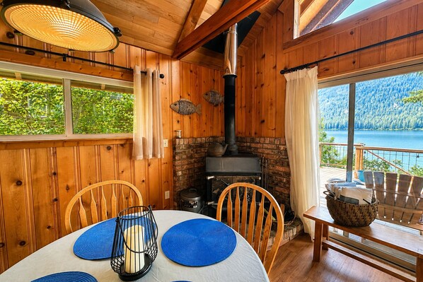 A wooden cabin with a fireplace, a dining table with blue placemats, and a view of a lake.