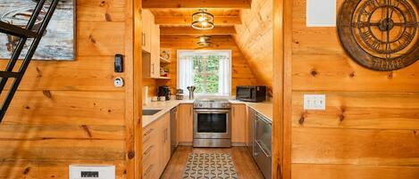 Interior de una cabaña de madera con cocina, un reloj y una escalera.