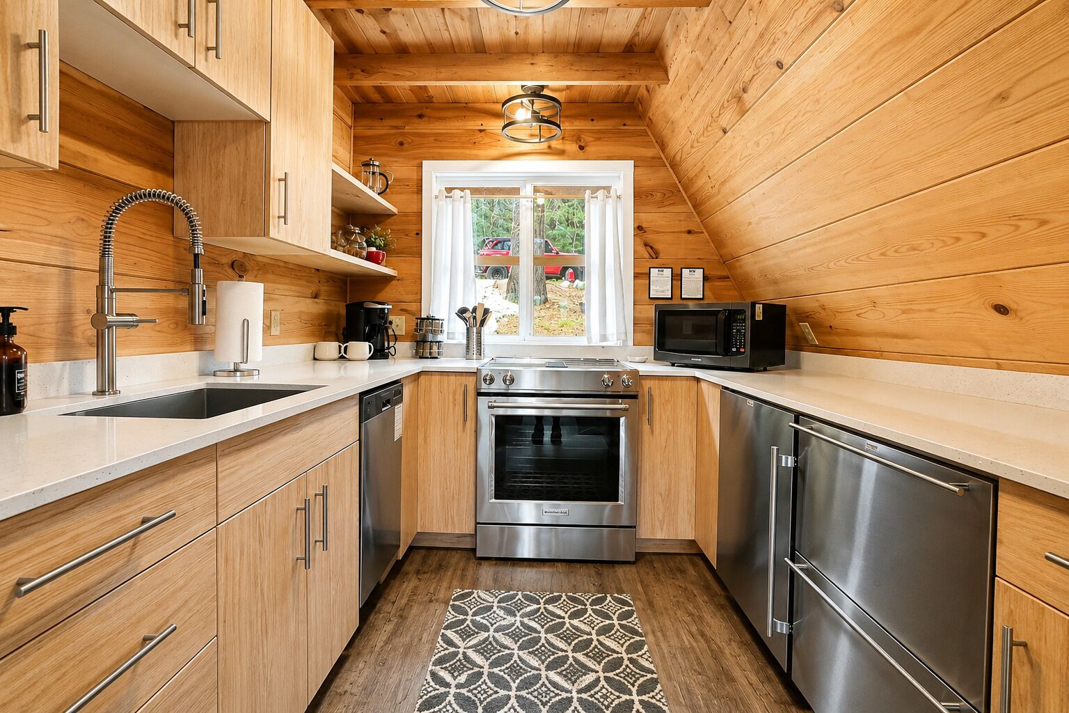 A compact kitchen with wooden cabinetry, stainless steel appliances, and a patterned rug.