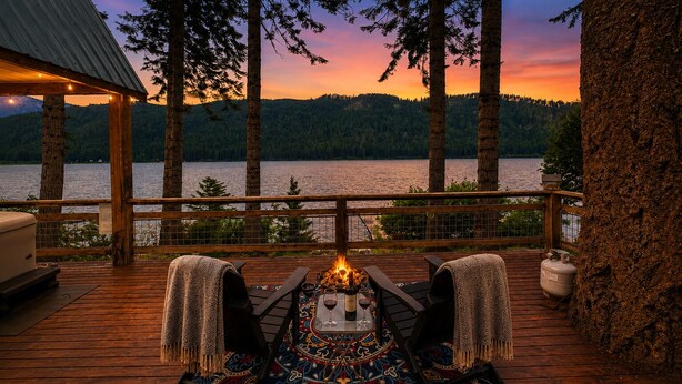 A wooden deck with a fire pit, outdoor seating, and a view of a lake at sunset. - Doc Roy's Legacy On Fish Lake Home by NW Comfy Cabins by RedAwning (Leavenworth)