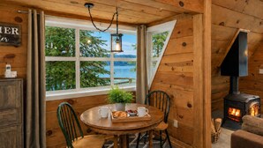 A cozy cabin interior with a wooden interior, a round dining table with chairs, a fireplace, and a window overlooking a lake. - Doc Roy's Legacy On Fish Lake Home by NW Comfy Cabins by RedAwning (Leavenworth)