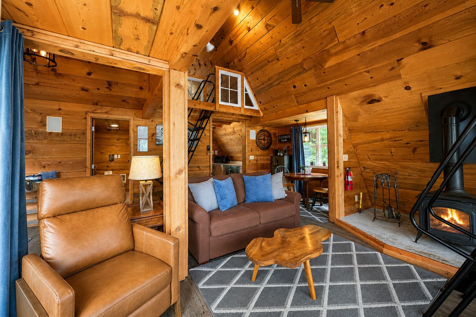 Un interior de cabaña acogedor con un sofá de cuero, una mesa de centro de madera, una chimenea y una escalera que sube a un nivel superior.