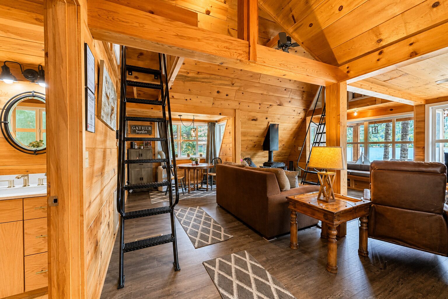 A wooden cabin interior with a loft bedroom, a dining area, and a living room.