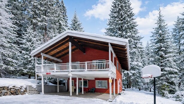 A two-story cabin with a balcony, surrounded by snow-covered trees.