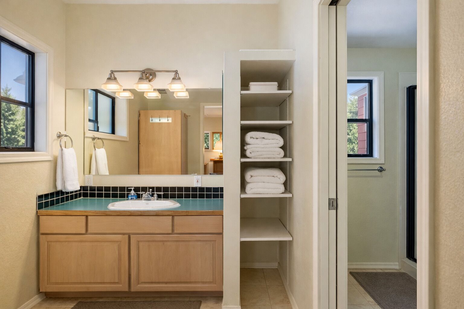 A bathroom with a double sink, a mirror, a towel rack, and a shelf with folded towels.
