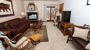 A cozy living room with a brown sofa, wooden coffee table, wicker chairs, a TV, and a fireplace.