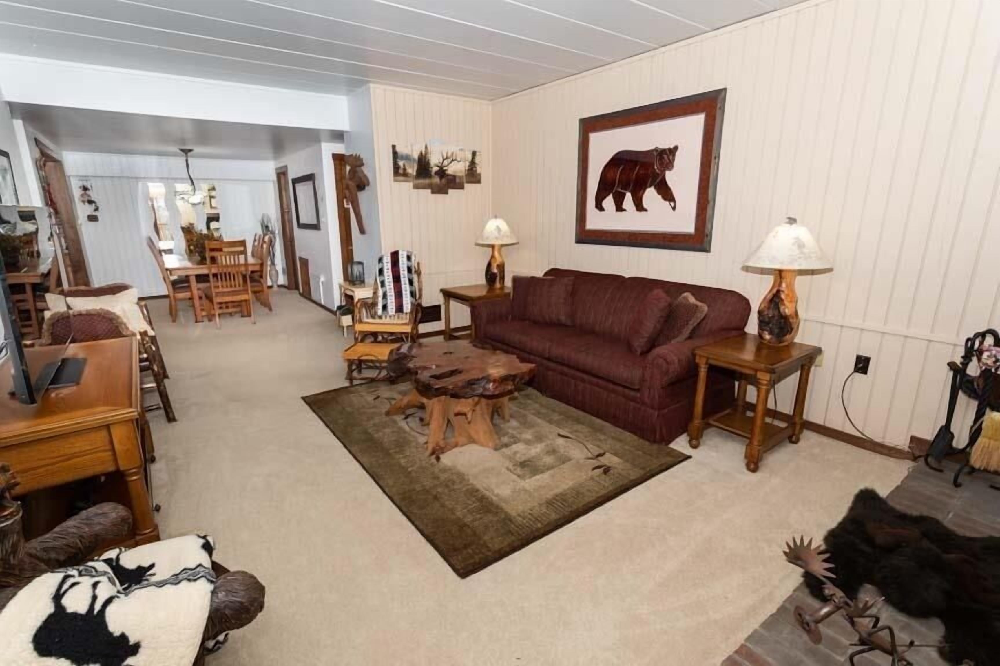 A living room with a red sofa, wooden coffee table, and a rug. There is a dining area with a wooden table and chairs.