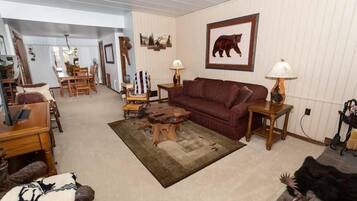 A living room with a red sofa, wooden coffee table, and a rug. There is a dining area with a wooden table and chairs.