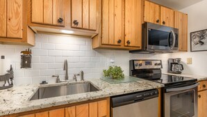 A modern kitchen with wooden cabinets, a stainless steel dishwasher, an oven, a microwave, and a granite countertop.