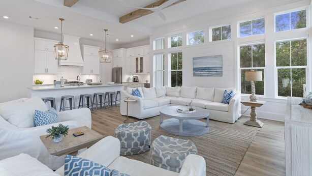 A spacious living room with a large white sectional sofa, a coffee table, and a kitchen area with white cabinets and a large island. - Blue Mountain Beach | Pool | Bikes (Santa Rosa Beach)