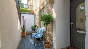 A narrow outdoor corridor with a bench, potted plants, and a door.