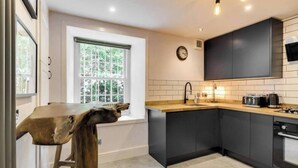 A modern kitchen with dark cabinets, a wooden countertop, and a window with a view of greenery.