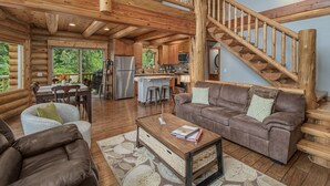 A spacious log cabin interior with a dining area, kitchen, and a wooden staircase. - Bearfoot Chalet 3 Bedroom Home by NW Comfy Cabins (Leavenworth)