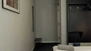 A hotel room with two beds, a framed picture on the wall, a coat rack, and a dark carpeted floor.