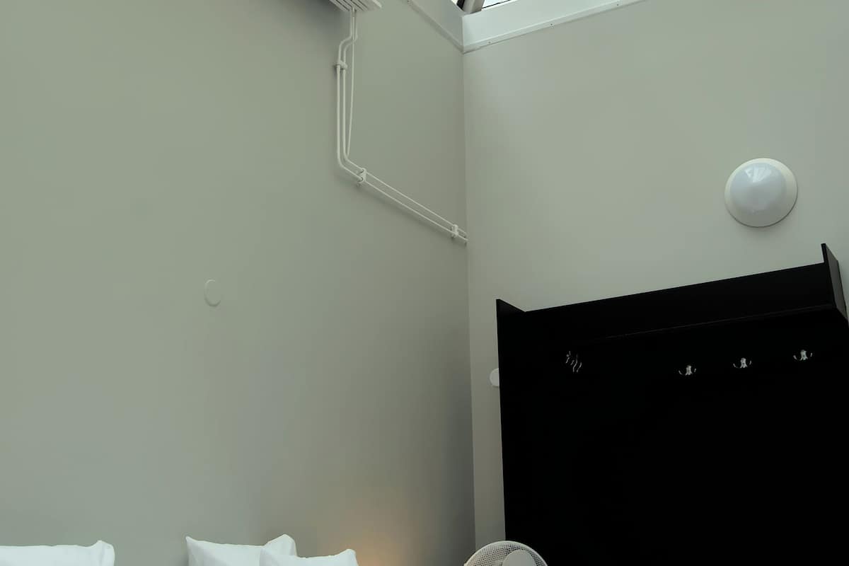 Ett modernt hotellrum med ett takfönster, en säng med vita sängkläder, en svart sänggavel och en bordsfläkt.