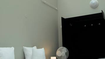 Ett modernt hotellrum med ett takfönster, en säng med vita sängkläder, en svart sänggavel och en bordsfläkt.