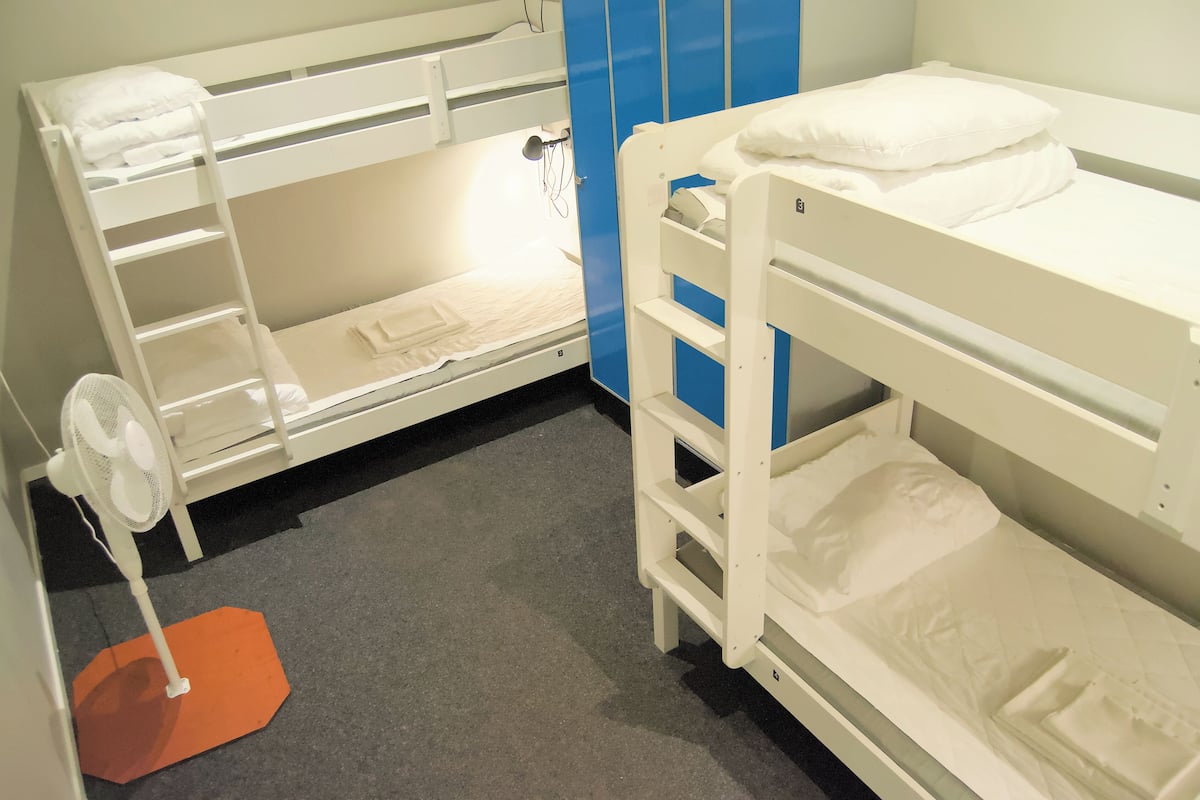 Ett rum med en våningssäng, en fläkt, en blå garderob och en liten orange matta.