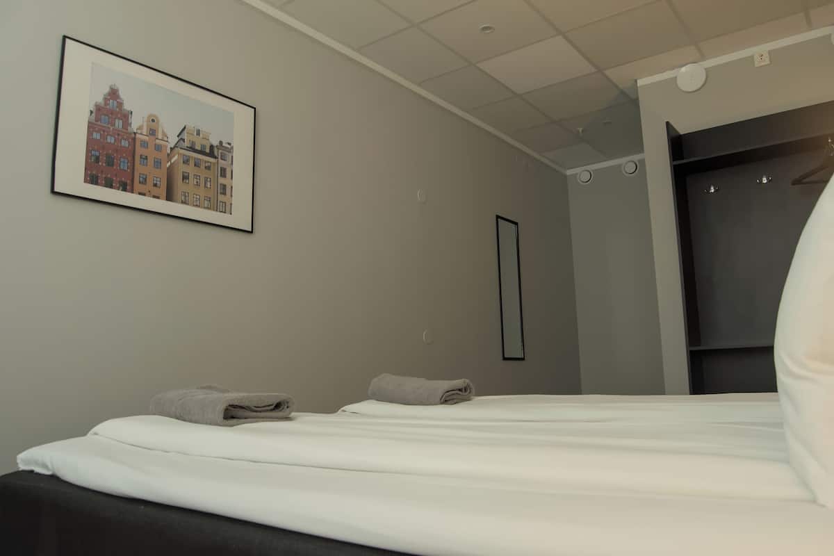 Ett hotellrum med en säng, en inramad bild av byggnader, en garderob och en spegel.