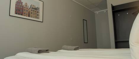 A hotel room with a bed, a framed picture of buildings, a wardrobe, and a mirror.