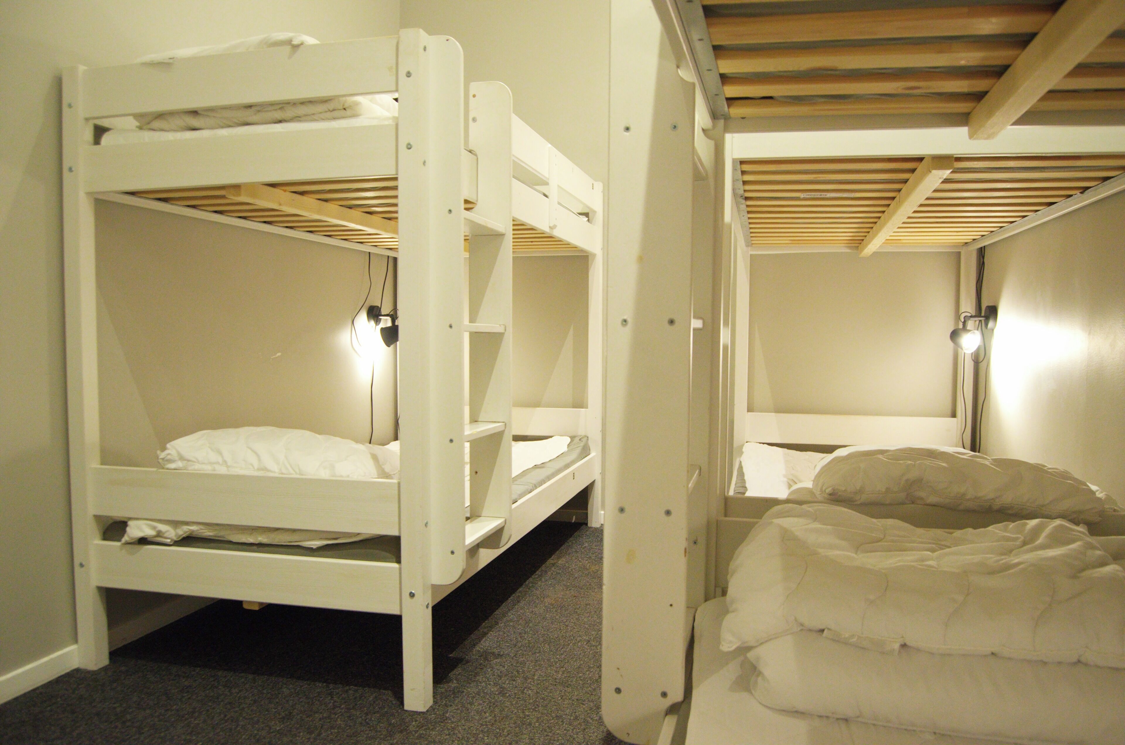 A bunk bed room with a wooden ceiling and a single bed with a white comforter.