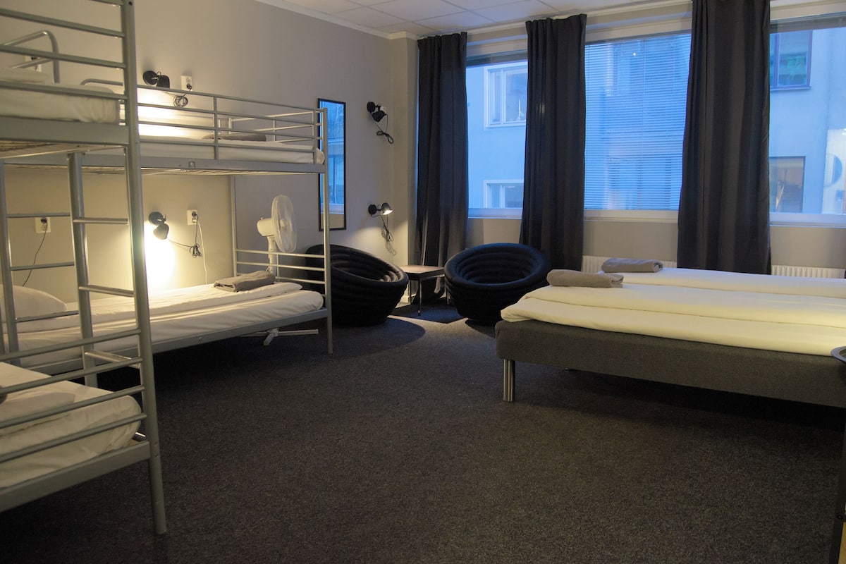 Ett hotellrum med våningssängar, ett skrivbord, en stol och ett fönster med gardiner.