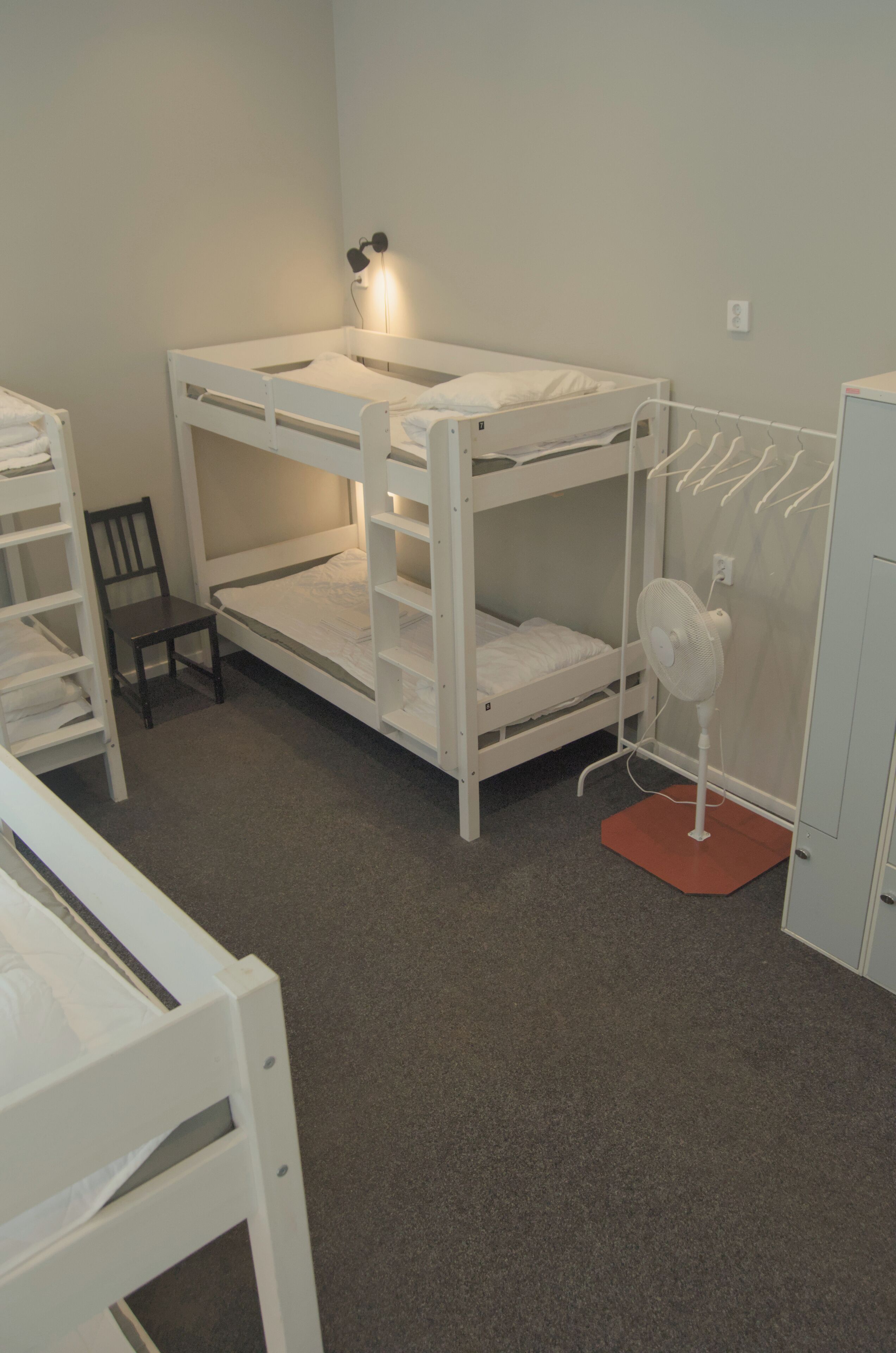 A bunk bed room with a desk, chair, and a standing fan.