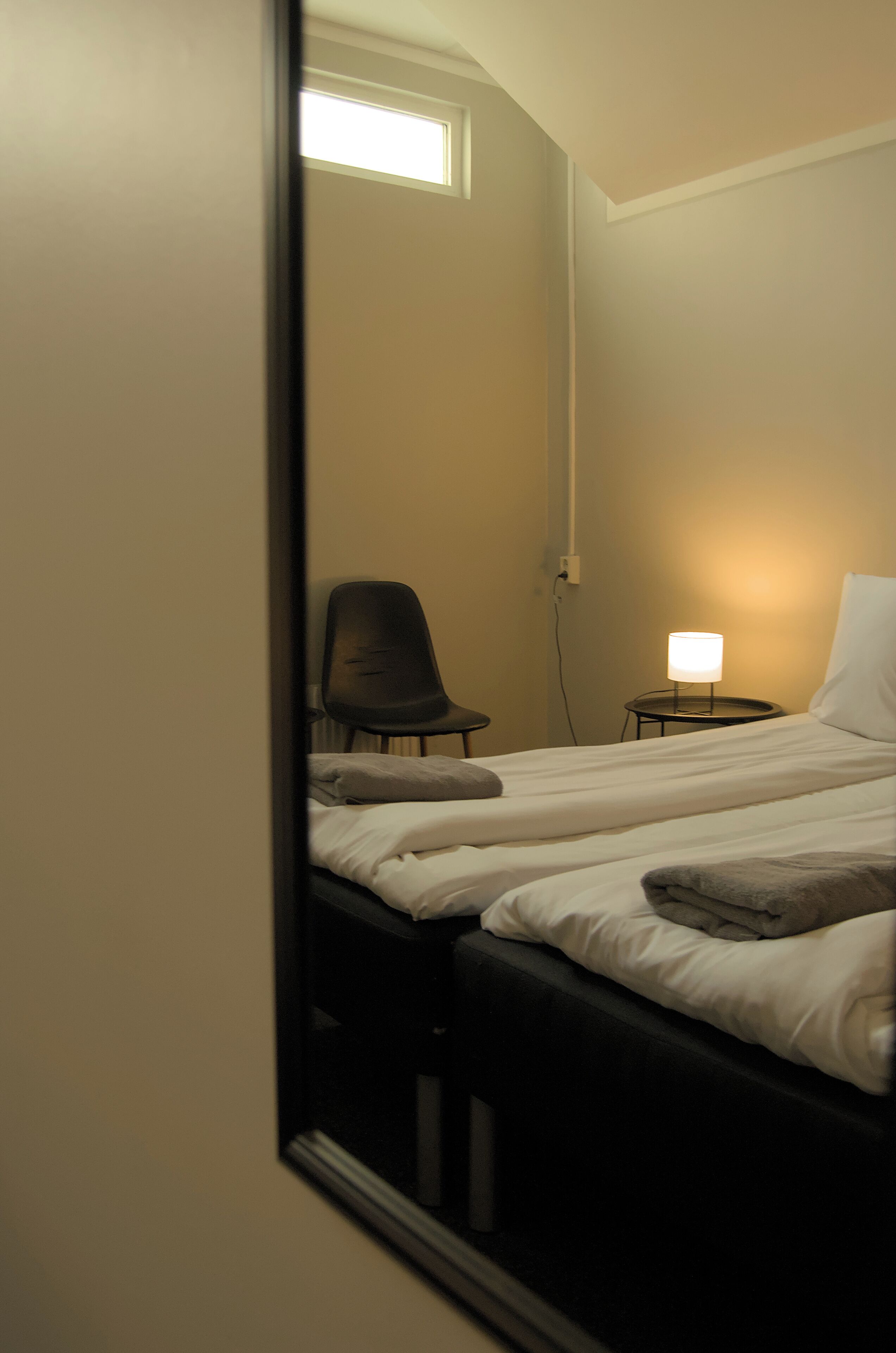 Une chambre d’hôtel avec un lit, une chaise, une table de chevet avec une lampe et une fenêtre.