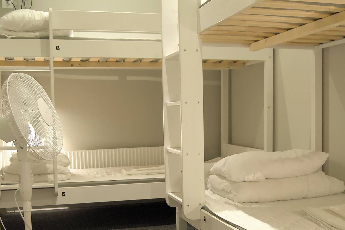 Ett rum med en våningssäng, en vit fläkt och en yogamatta på golvet.
