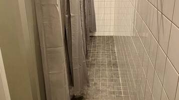 A narrow bathroom with tiled walls and floor, a metal shower drain, and a row of hanging shower curtains.
