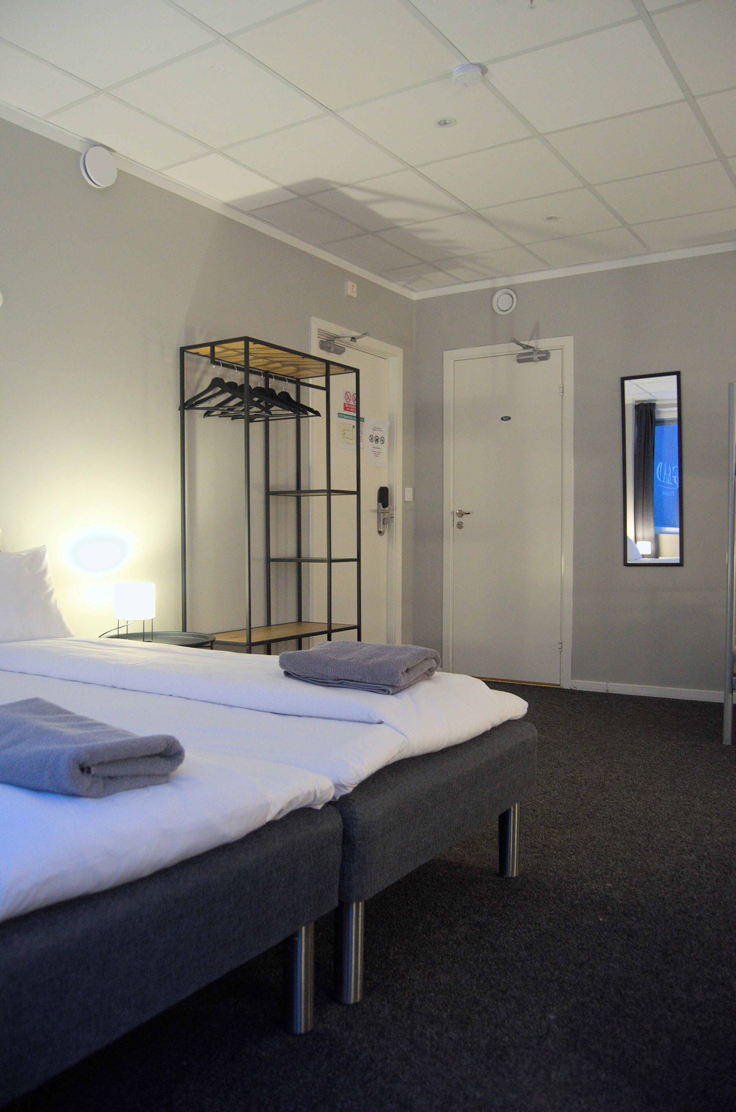 Hotellihuone, jossa on sänky, vaatekaappi, peili ja ovi.