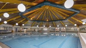 Ein Innenpool mit hoher Decke und gelben Balken, umgeben von weißen Wänden und einem gefliesten Boden.
