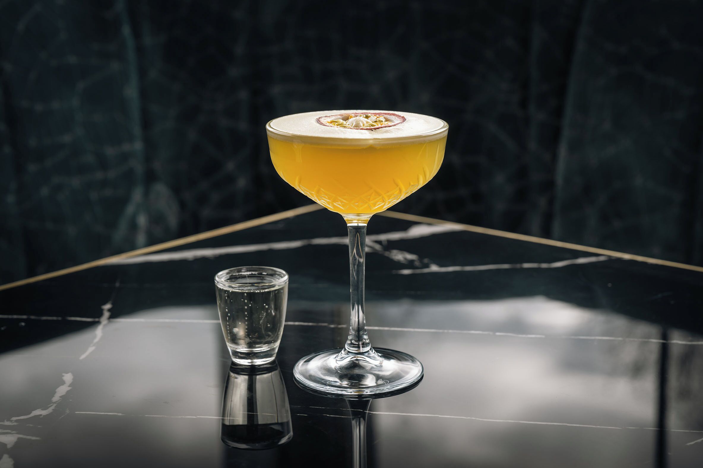 A cocktail in a stemmed glass on a reflective surface.