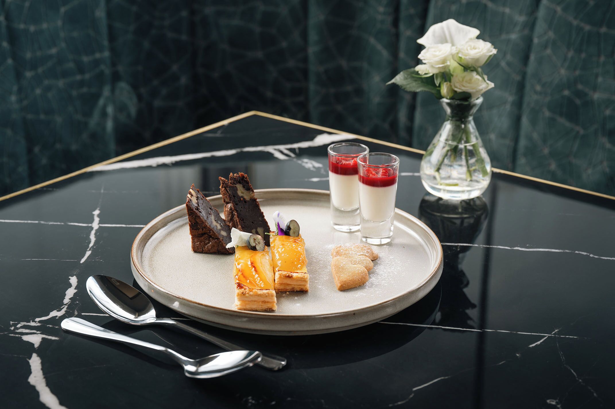 A dessert plate with various sweets and two glasses of a red dessert on a marble table.