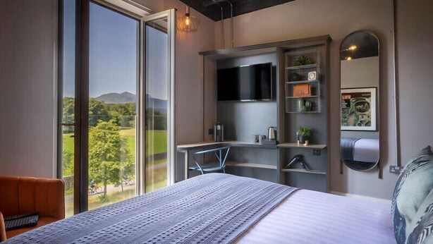 Ein Schlafzimmer mit großem Fenster, einem Bett, einem Fernseher und einem Spiegel.