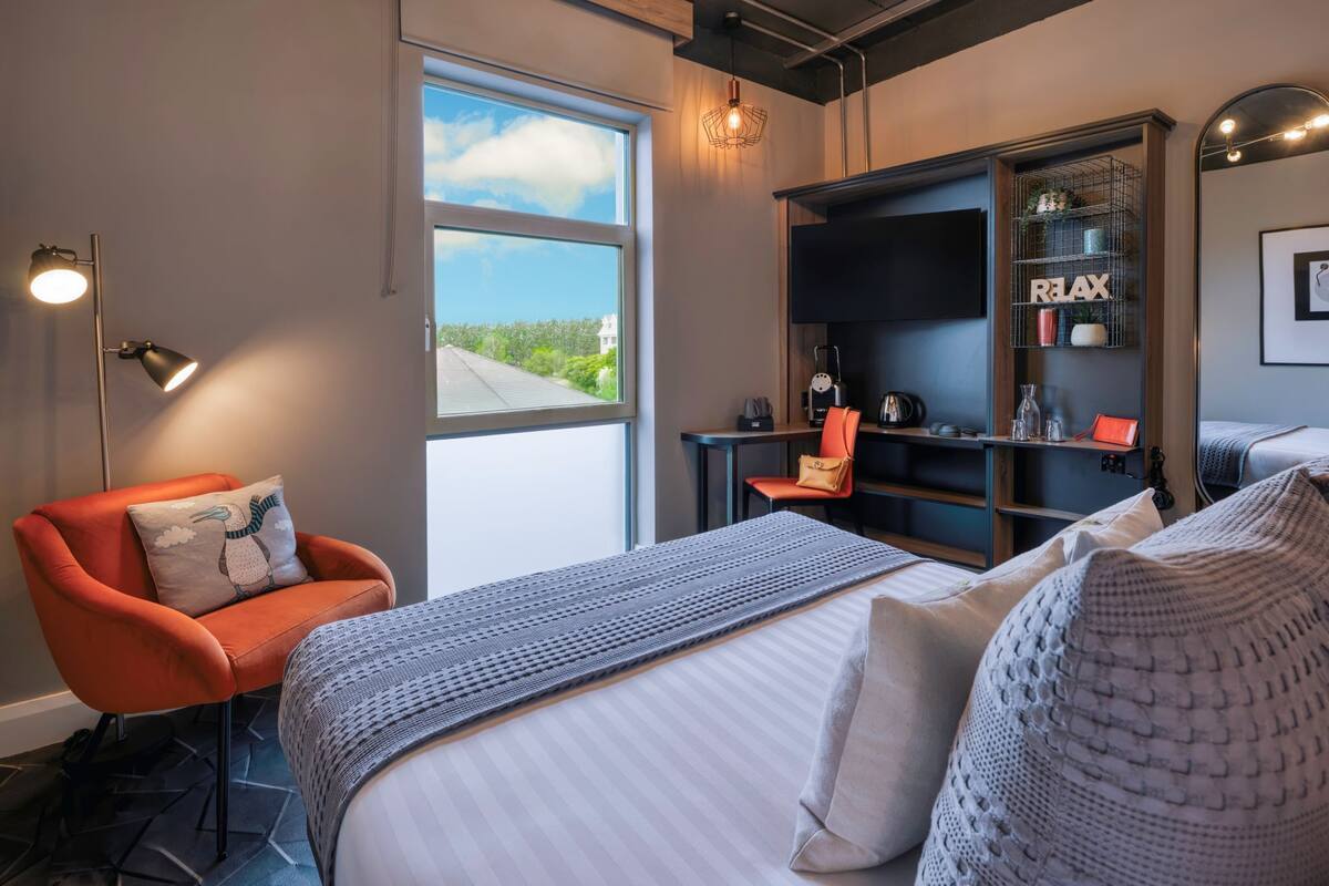 Una habitación de hotel moderna con una cama grande, un escritorio, una silla y una estantería.