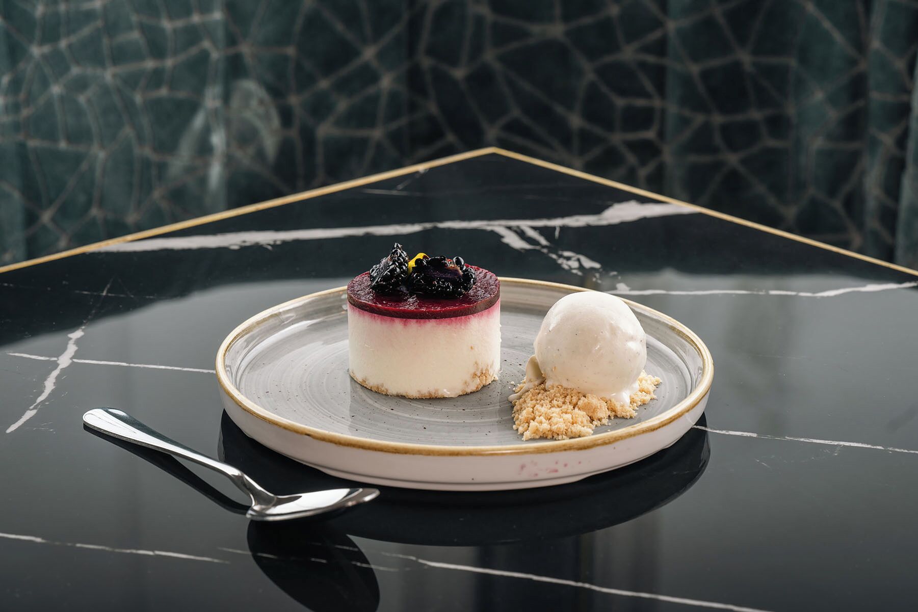 A dessert on a plate with a spoon, set on a reflective black table with a geometric pattern in the background.