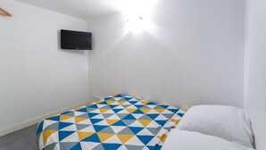 Een kleine, eenvoudig ingerichte kamer met een bed, een flatscreen televisie aan de muur en één lamp.