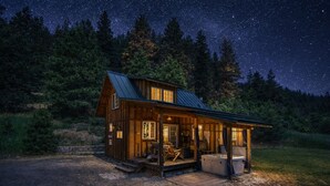 A rustic cabin with a porch, a hot tub, and a starry night sky.