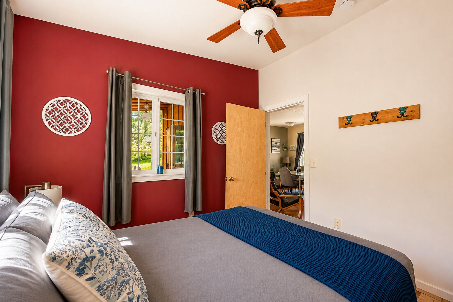 Un dormitorio con cama, ventilador de techo, ventana con cortinas y puerta que da a otra habitación.