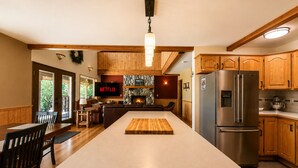 A spacious kitchen with wooden cabinets, a large island, a built-in fireplace, and a stainless steel refrigerator.