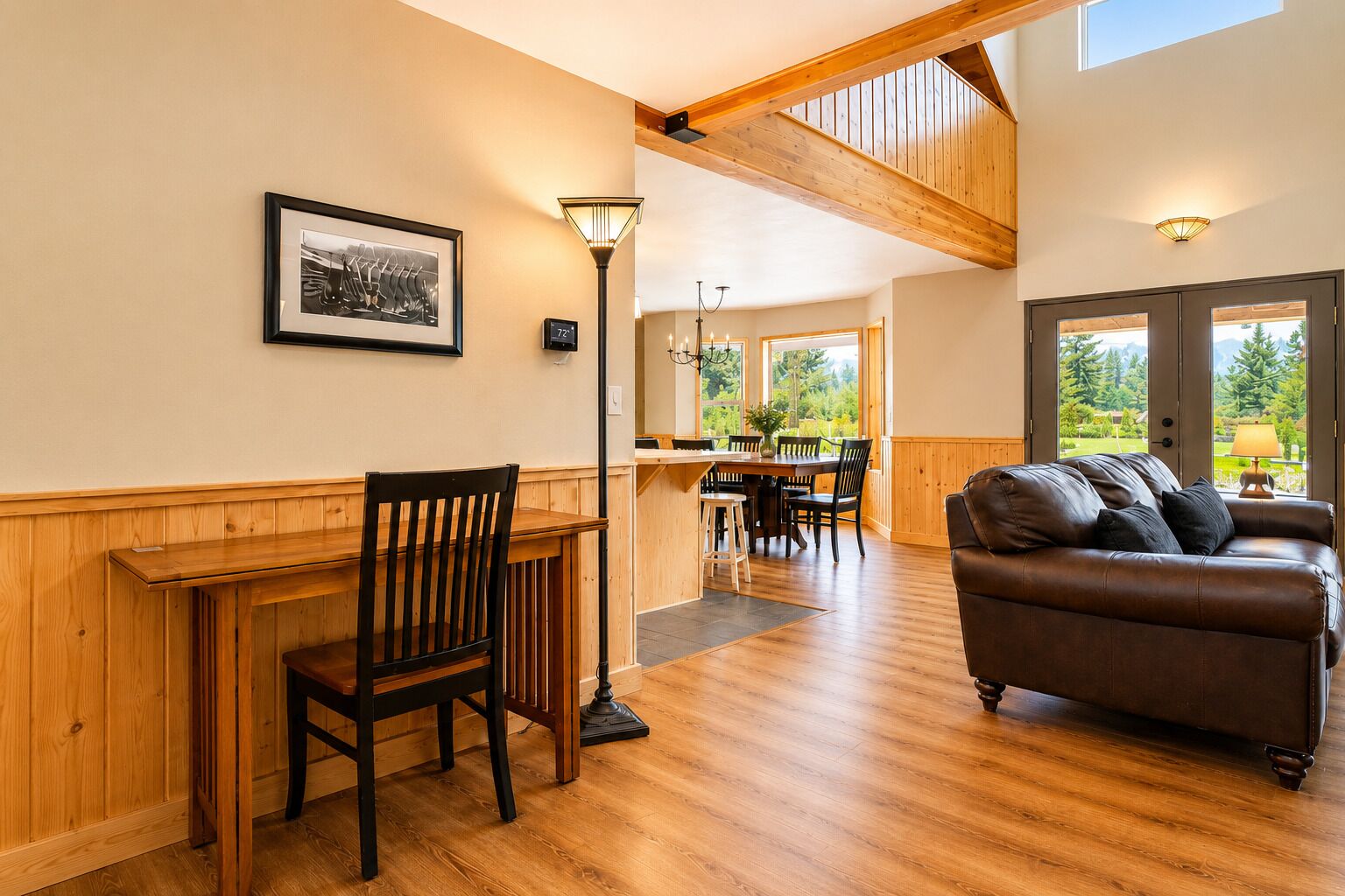 A room with a wooden dining table, a leather sofa, and a view through large windows.