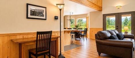 A room with a wooden dining table, a leather sofa, and a view through large windows.
