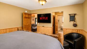 A bedroom with a large bed, a TV, a wooden wardrobe, a chair, and a bathroom visible through an open door.