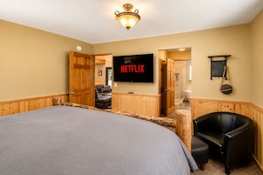 Een slaapkamer met een groot bed, een televisie, een houten garderobe, een stoel, en een zichtbare badkamer door een geopende deur.