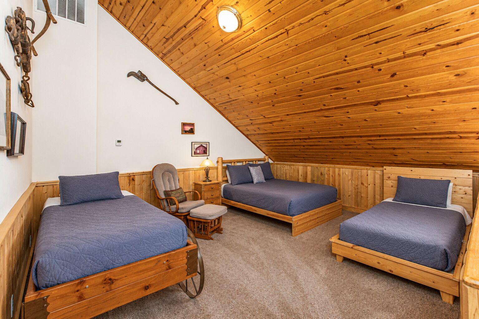 Une pièce avec trois lits en bois, un fauteuil à bascule et une petite table avec une lampe.